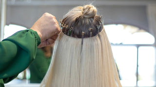 A stylist installing a row of weft extensions on long blonde hair, with sectioning clips along the crown