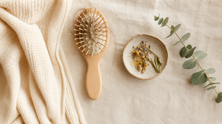 Flat-lay: hair brush with strands on cream linen, eucalyptus and dried botanicals