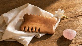 Sandalwood gua sha tool on folded cream silk with jasmine flower and rose quartz