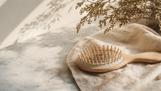 Wooden hair brush with strands on cream linen, soft botanical accent