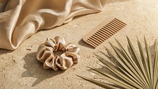 Champagne silk scrunchie and detangling comb on travertine with dried palm leaf